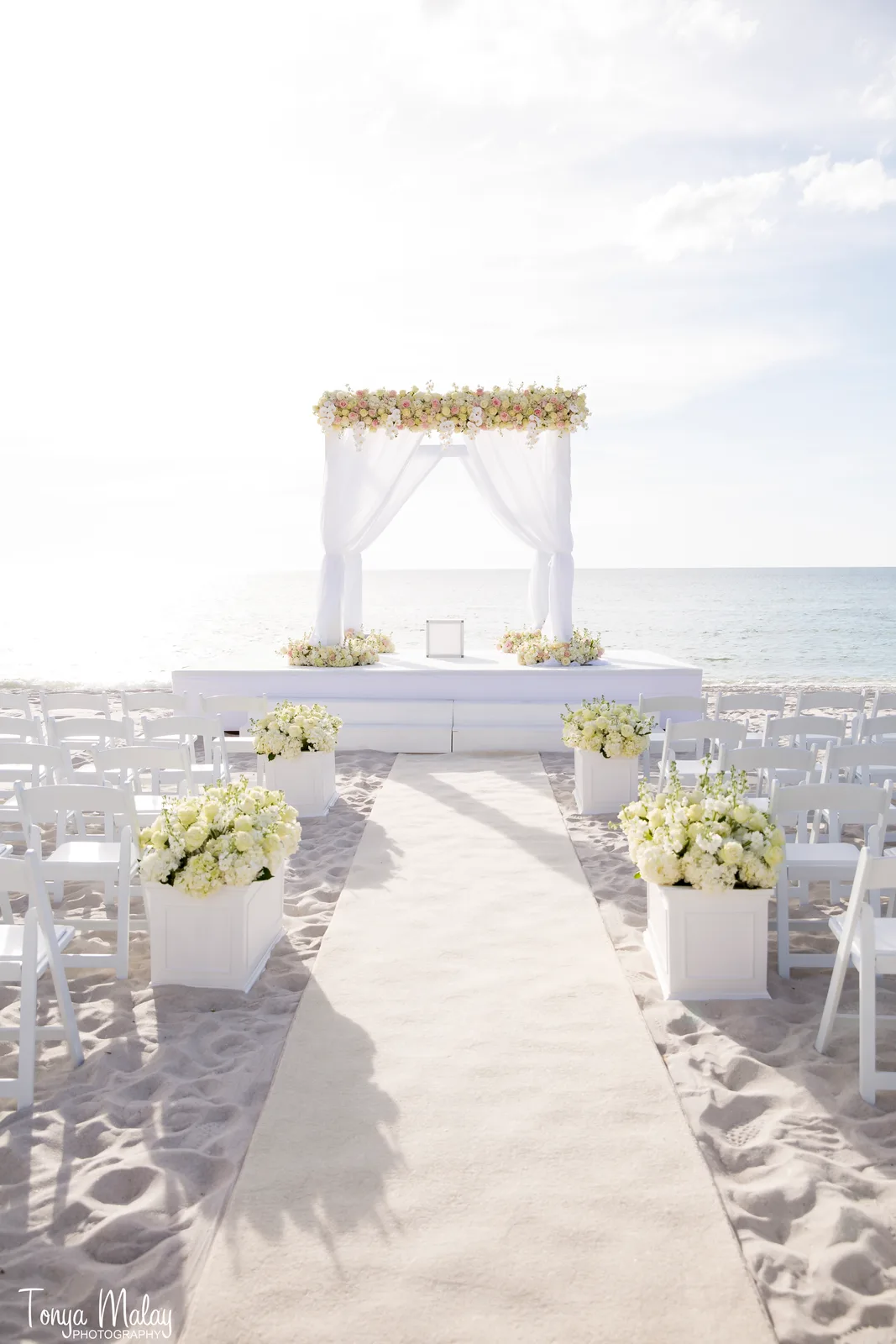 White ceremony cabana with champagne florals on the sand