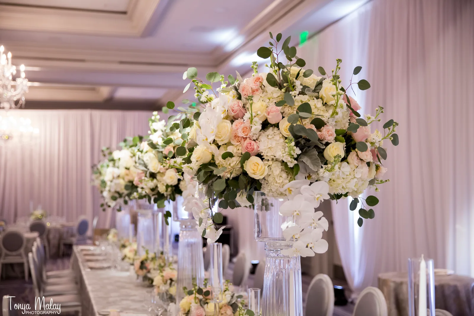 Long reception table under crystal chandeliers with tall centerpieces