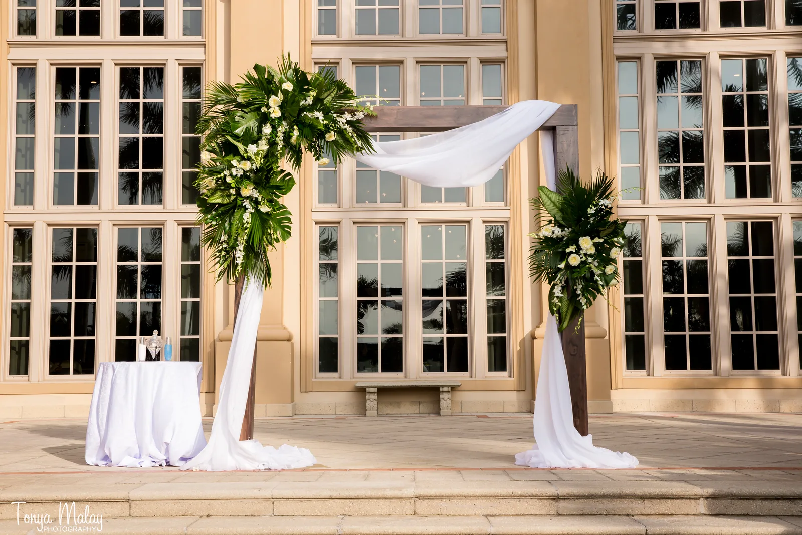 Wedding arbor with greenery and white florals set against a grand resort facade