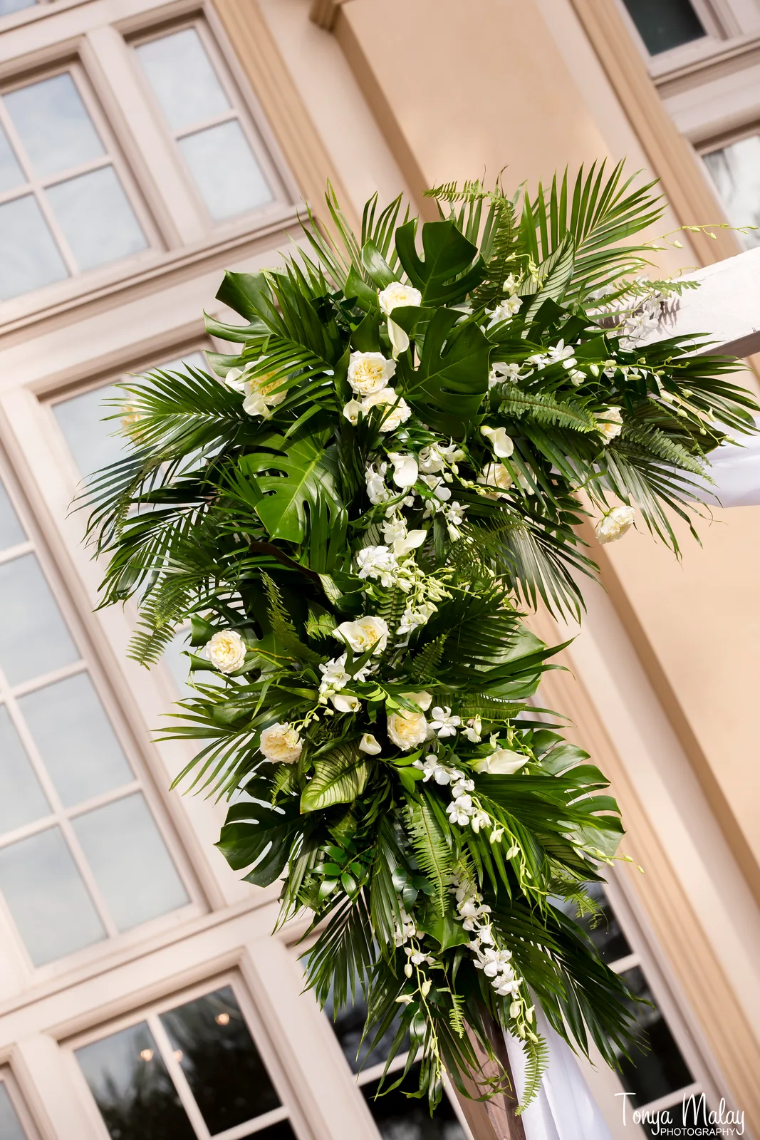 Cascading white orchid and tropical foliage spray on an arbor post
