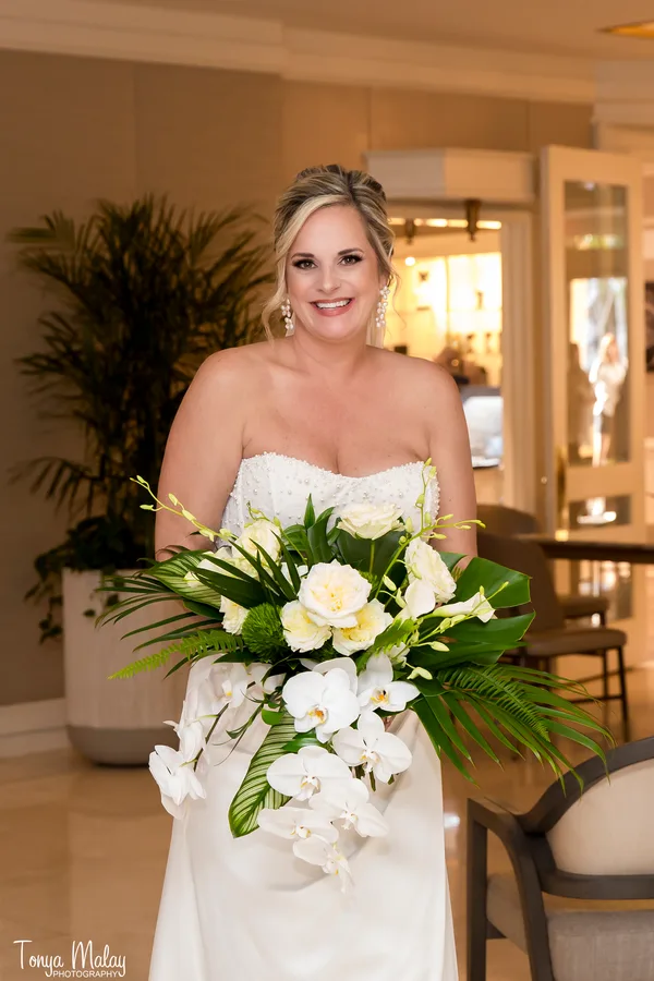 Bride carrying a cascading white orchid and palm bouquet