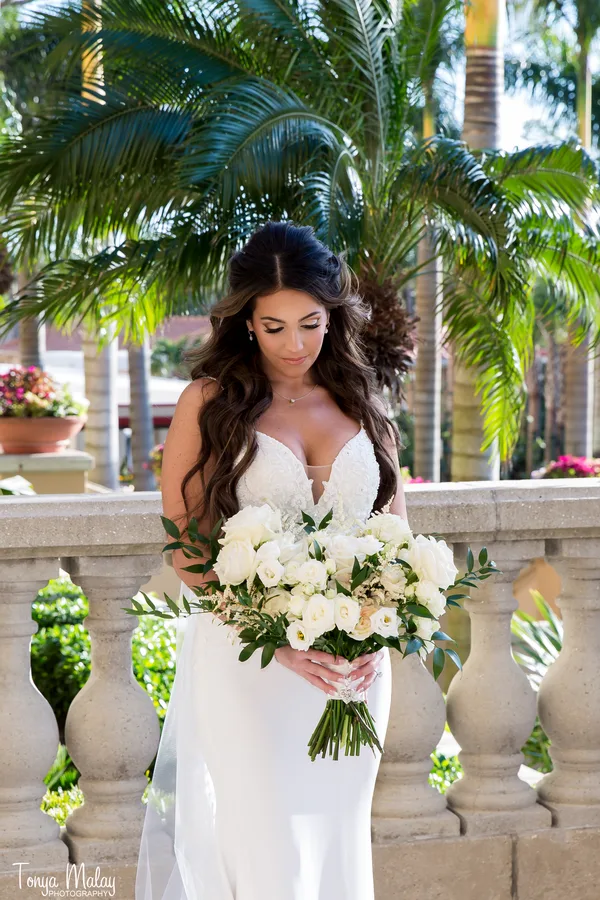 Bride holding a white garden rose bouquet beneath palm trees