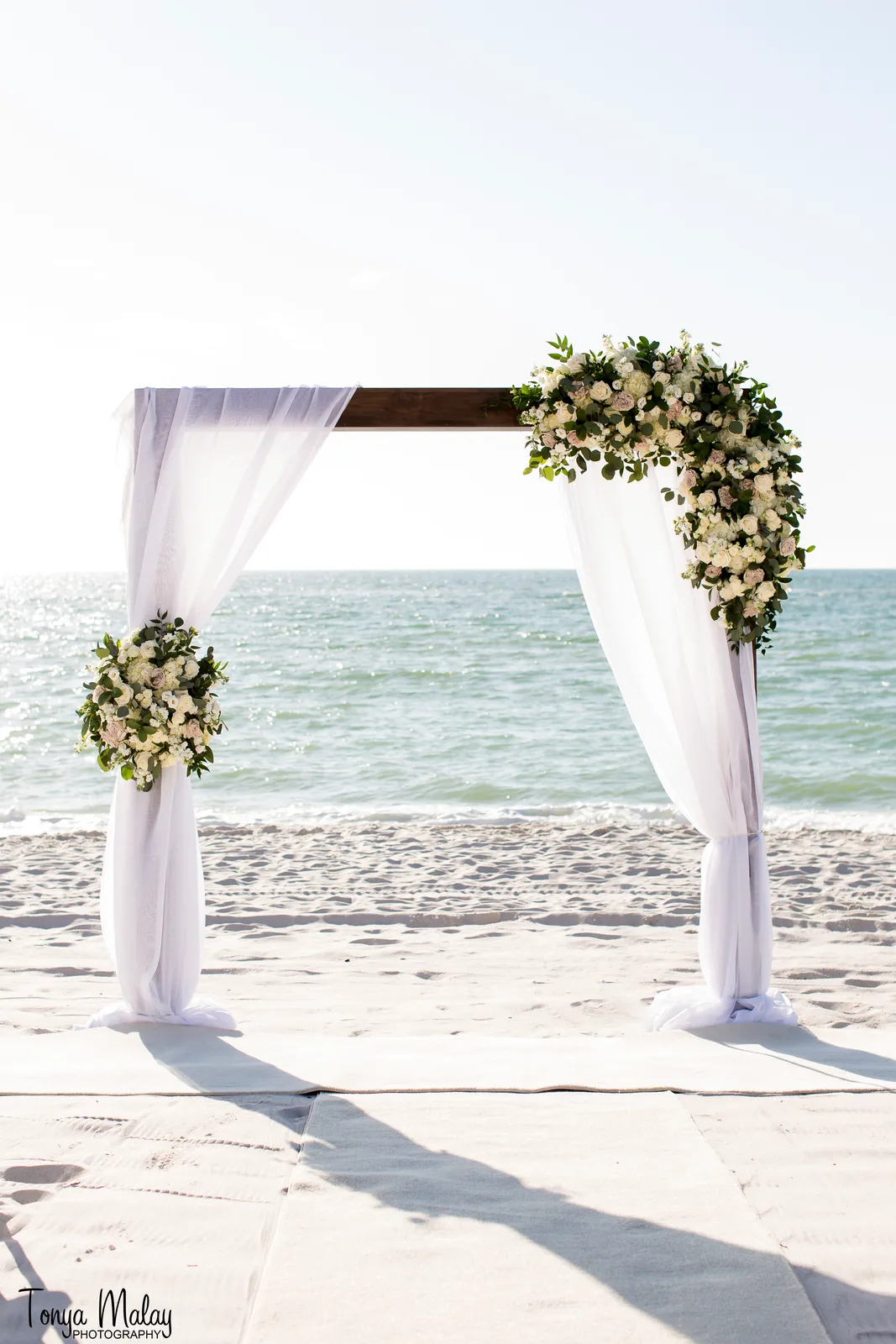 Draped wedding arch with white floral spray at the shoreline