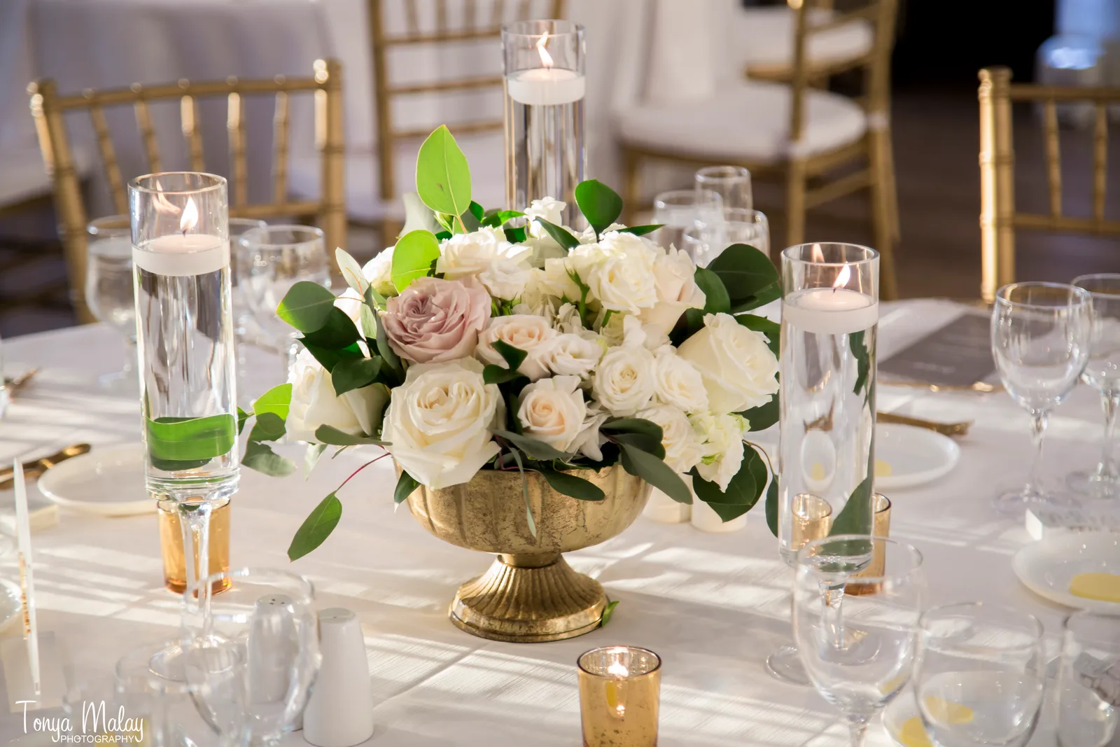 Gold chiavari chairs and centerpieces along a long white reception table