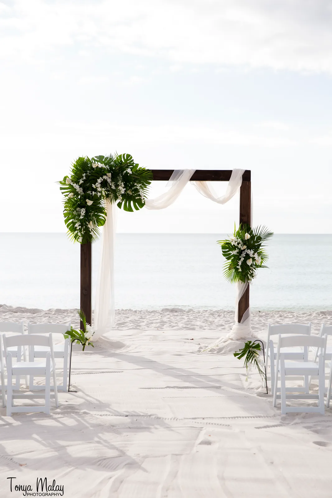 Dark wood beach arbor with white drape and tropical white florals