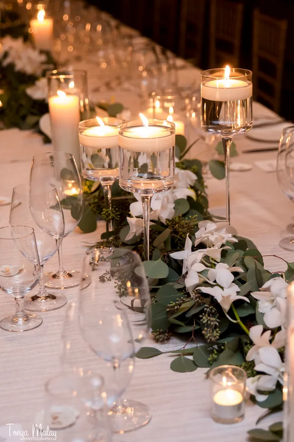 Floating candles and greenery garland with white orchids on an intimate dinner table