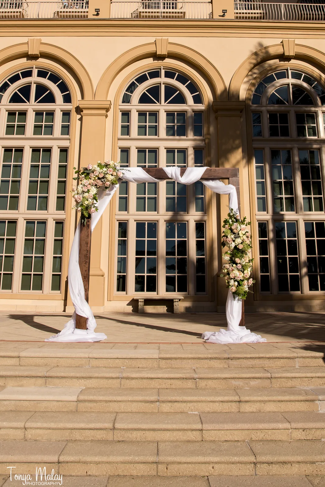 Draped ceremony arch with blush rose sprays before arched windows at golden hour