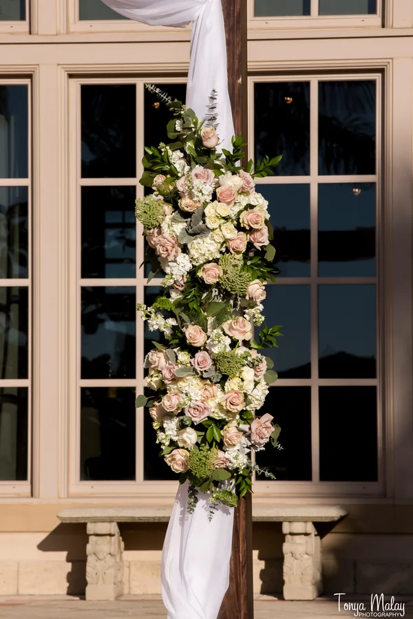 Blush rose garland climbing a dark wood ceremony post