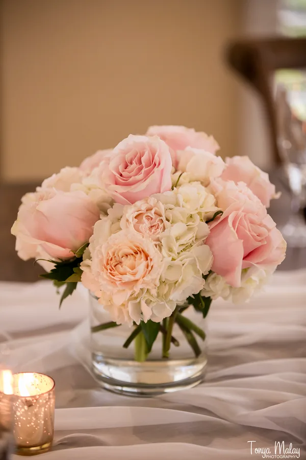 Hand-tied posy of blush roses and white hydrangea in a clear glass vase beside a candle