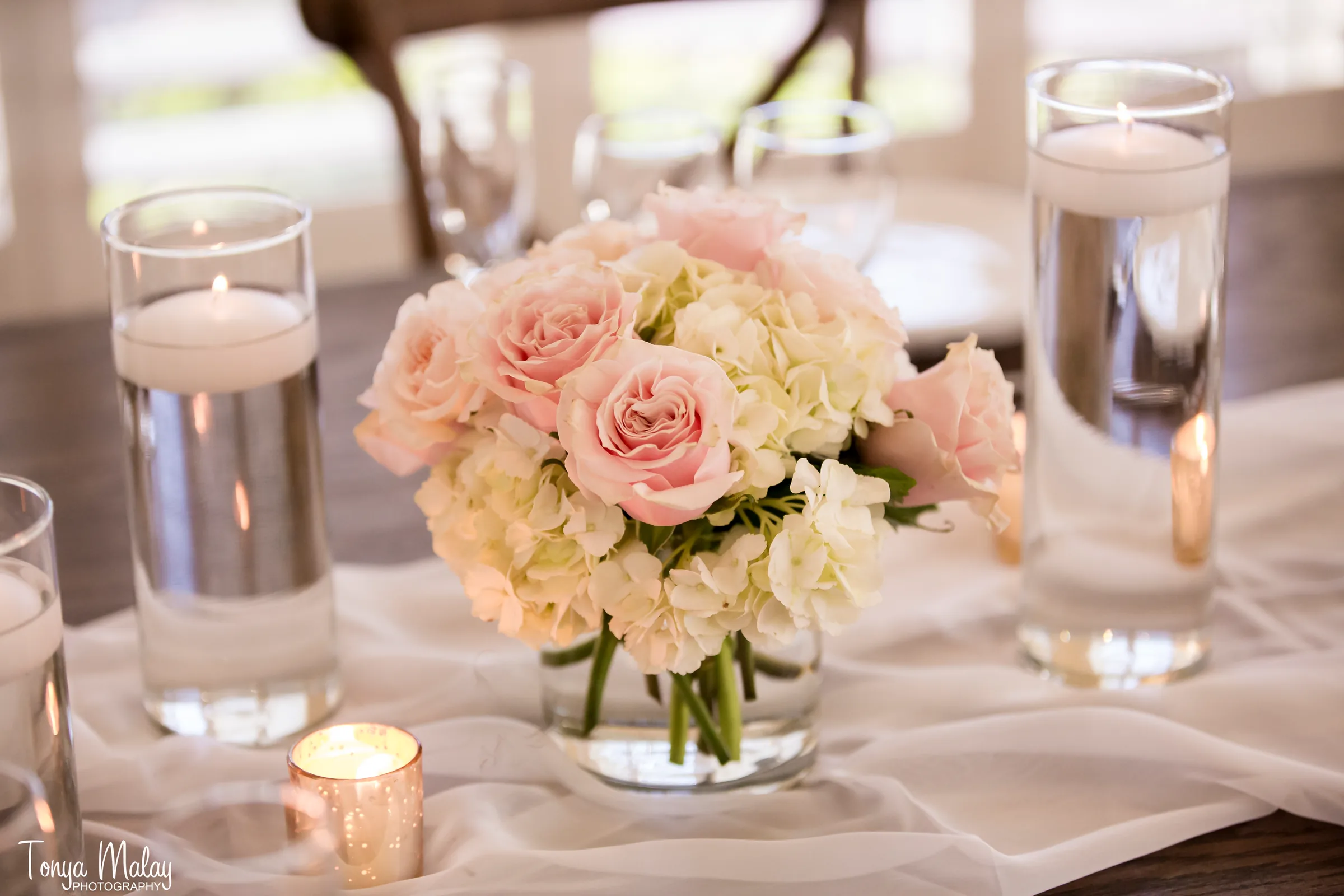 Floating candles and a blush posy along a sheer table runner at a candlelit reception