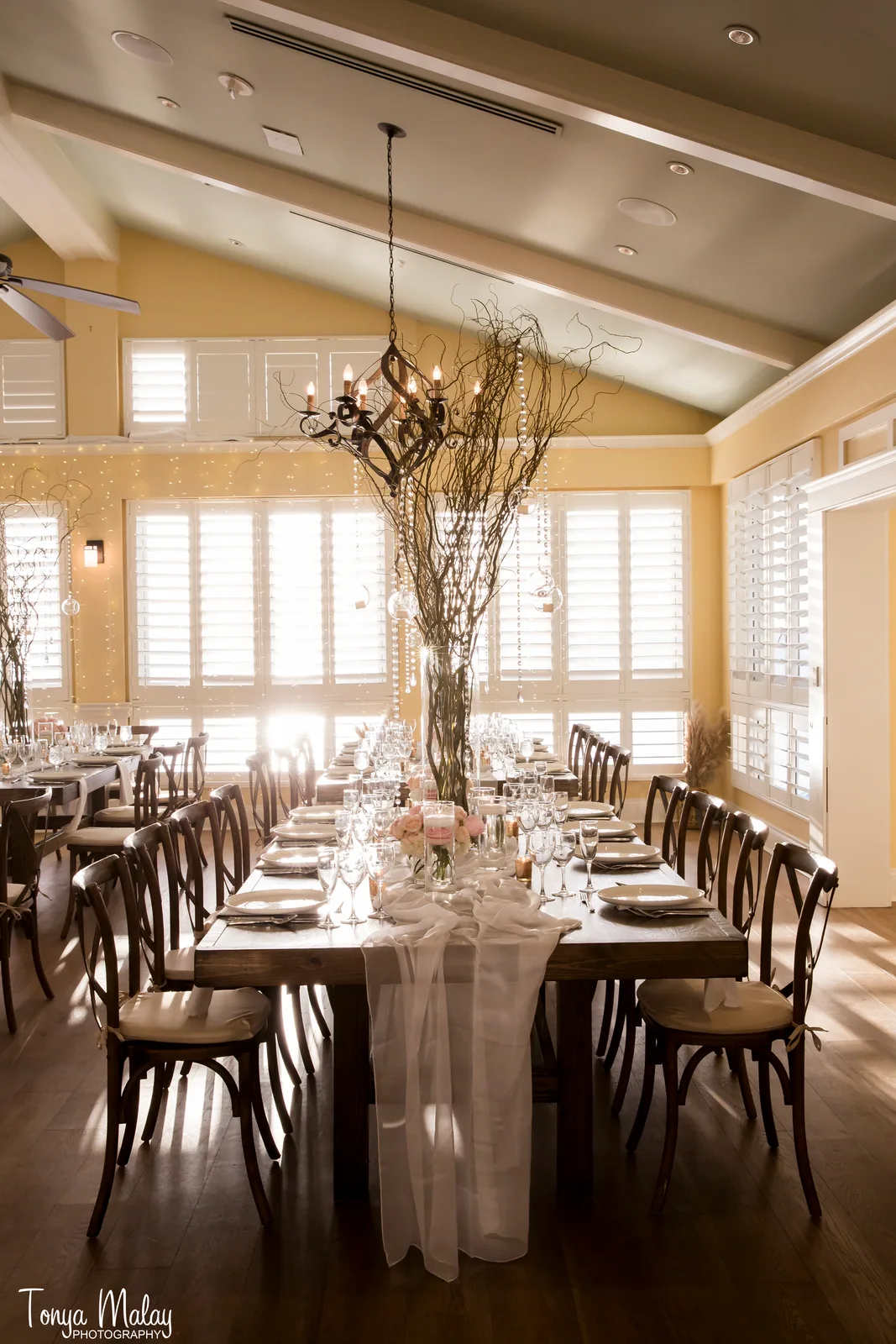 Farm table with willow branch centerpiece, sheer runner, and hanging votives